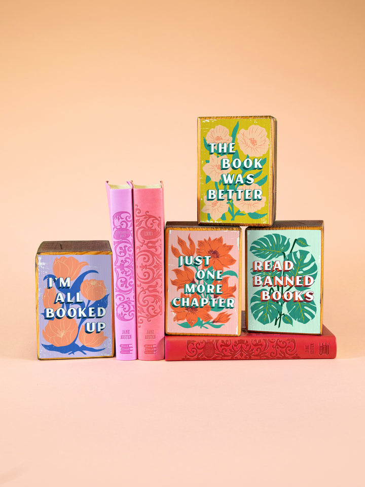 stack of four wood bookends featuring colorful flower illustrations with bookish sayings, "I&