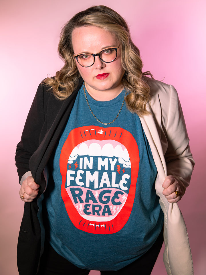Lindsey Archer modeling  teal crew neck unisex t-shirt with lips, open mouth red lips illustration and saying, "In my female rage era," under color blocked black and white plus size blazer