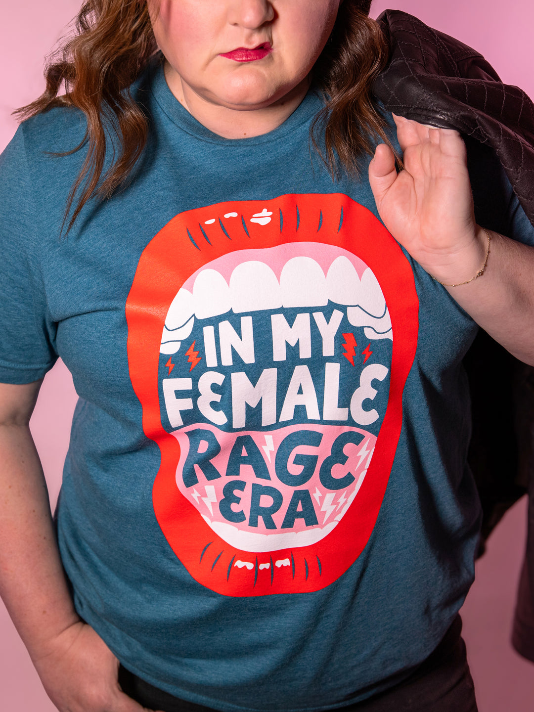 teal crew neck t-shirt with lips, open mouth red lips illustration and saying, "In my female rage era." Kristen modeling shirt with mouth in snarl.