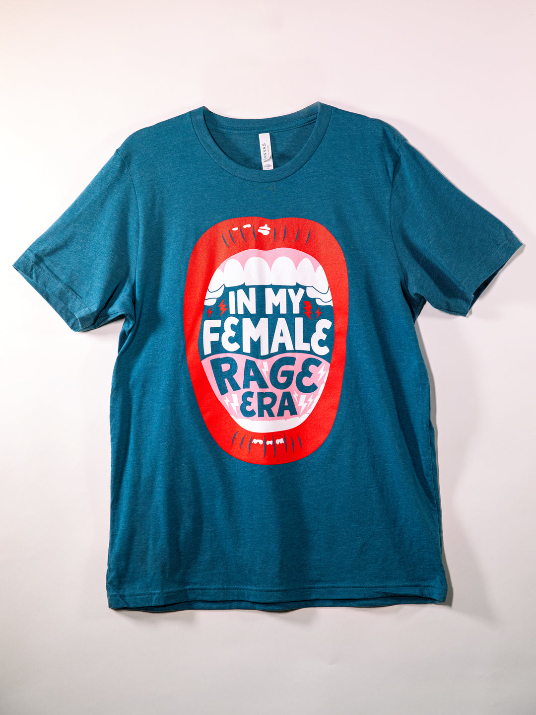 teal crew neck t-shirt with lips, open mouth red lips illustration and saying, "In my female rage era." flat, on white background