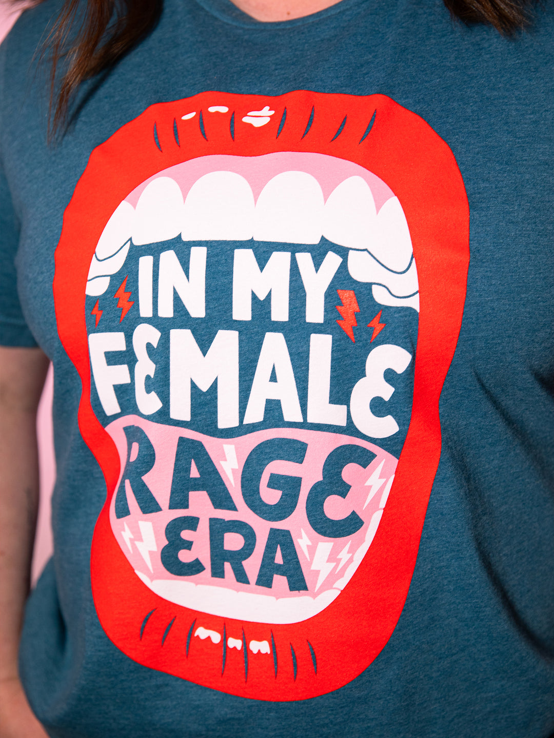 close up view of  screenprinted graphic  with lips, open mouth red lips illustration and saying, "In my female rage era." on teal crew neck unisex t-shirt