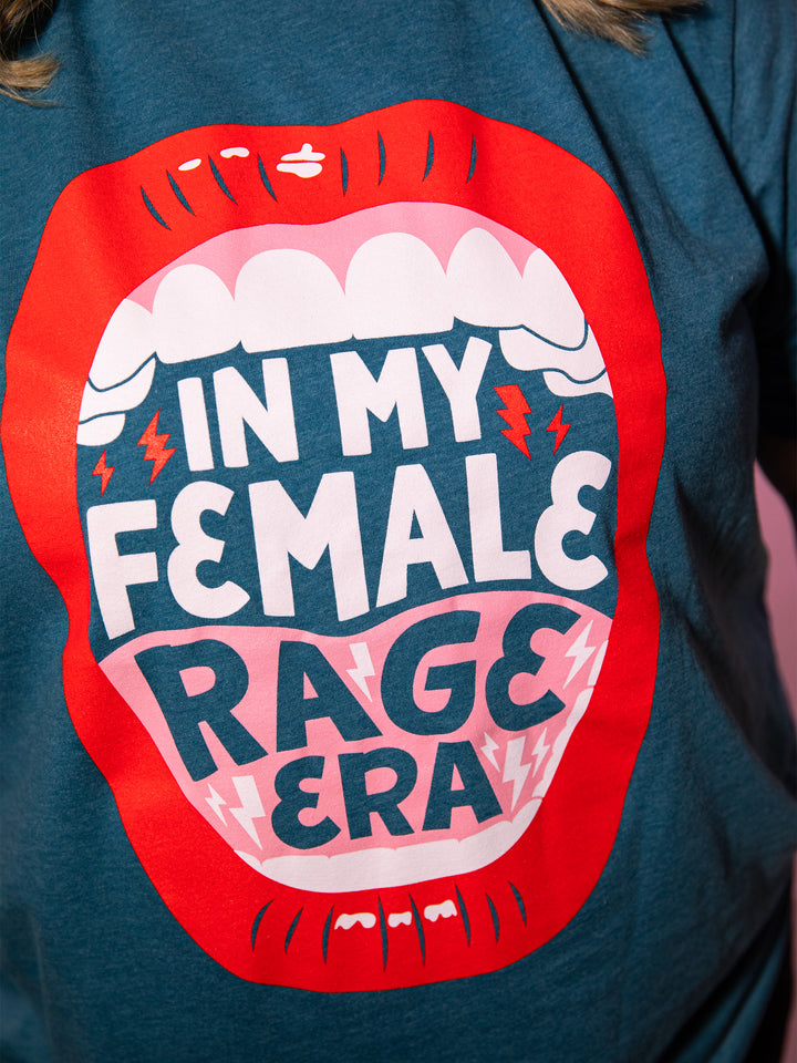 close up view of screen-printed graphic  with lips, open mouth red lips illustration and saying, "In my female rage era." on teal crew neck unisex t-shirt
