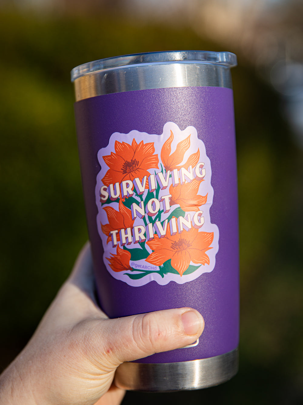 Surviving not thriving floral sticker on purple yeti cup in woman's hand