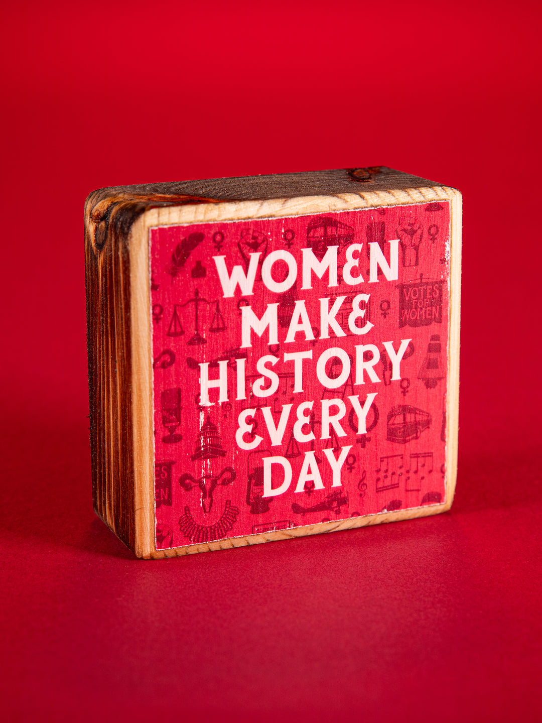 Red wood block that says "Women Make History Every Day" on a red background