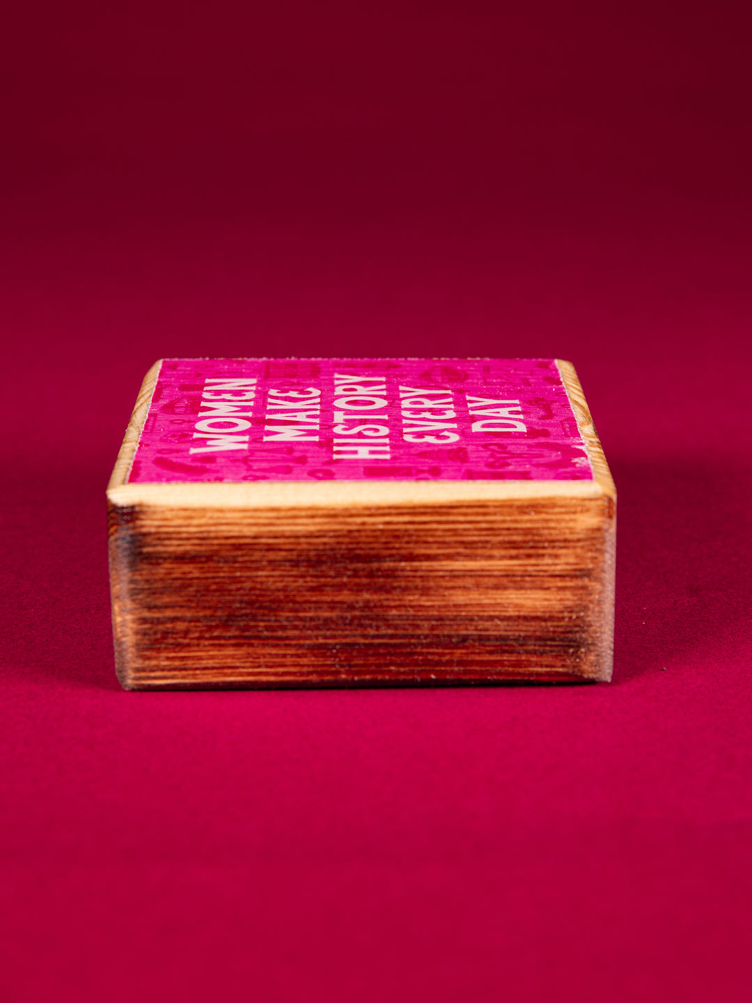 Side view of a stained wood block that says "Women Make History Every Day" on a dark pink background