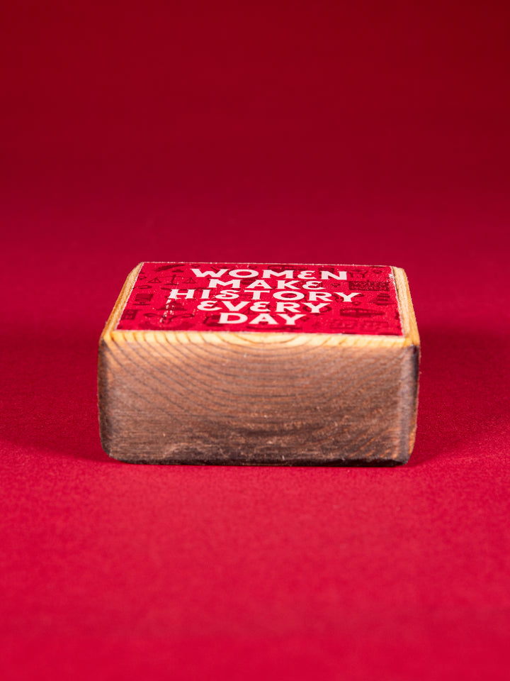 Bottom view of a Red wood block that says "Women Make History Every Day" on a red background