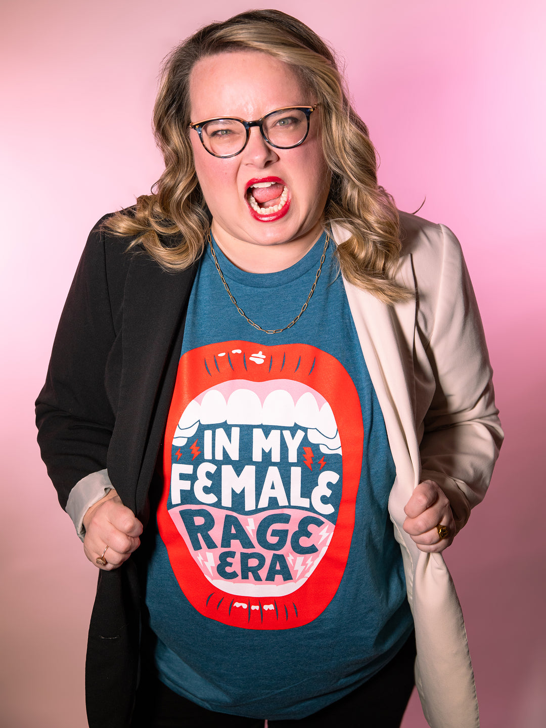 Lindsey Archer modeling  teal crew neck unisex t-shirt with lips, open mouth red lips illustration and saying, "In my female rage era," underneath black and white plus size color block blazer