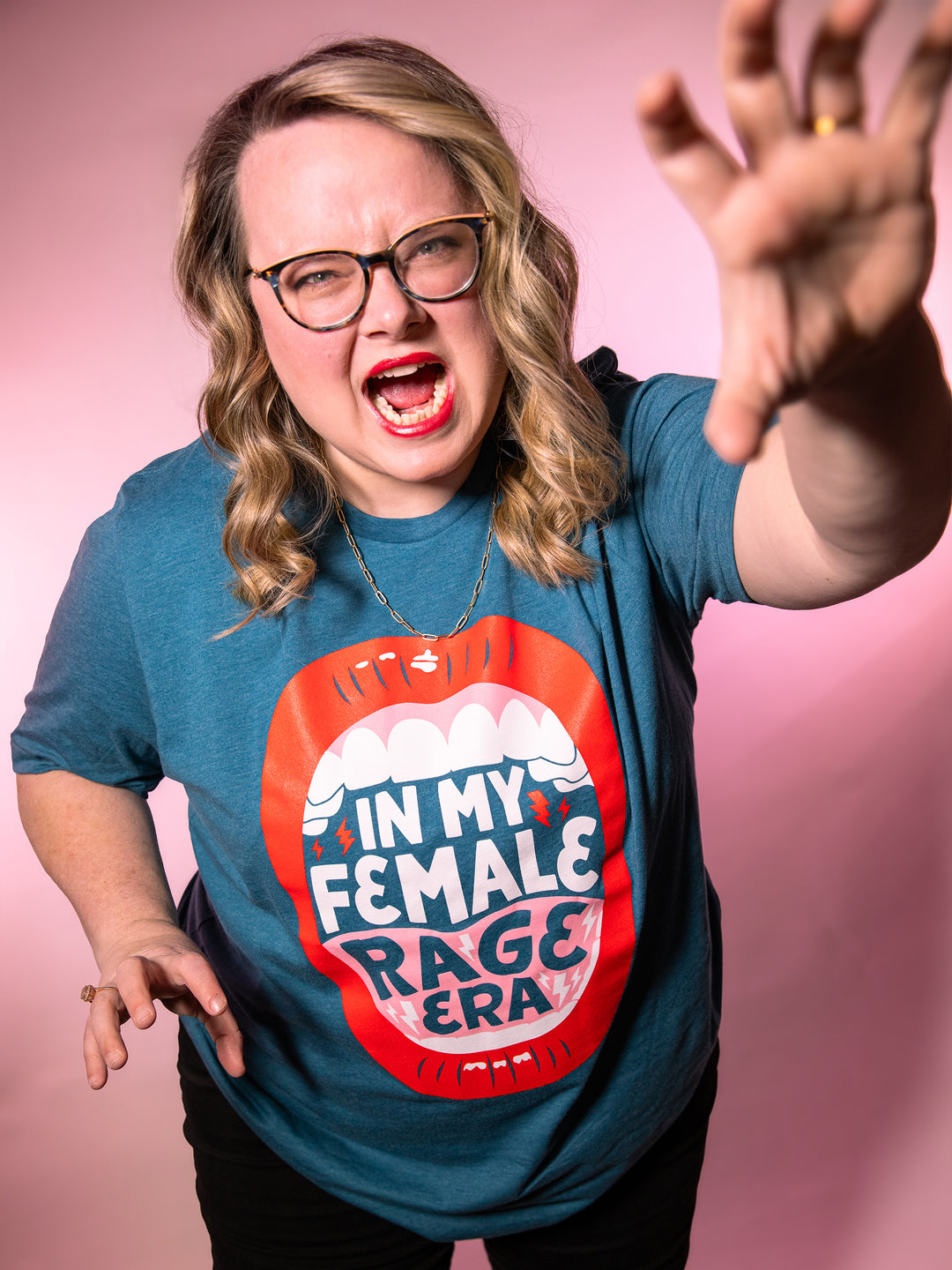 Lindsey Archer modeling feminist apparel;  teal crew neck unisex t-shirt with lips, open mouth red lips illustration and saying, "In my female rage era."