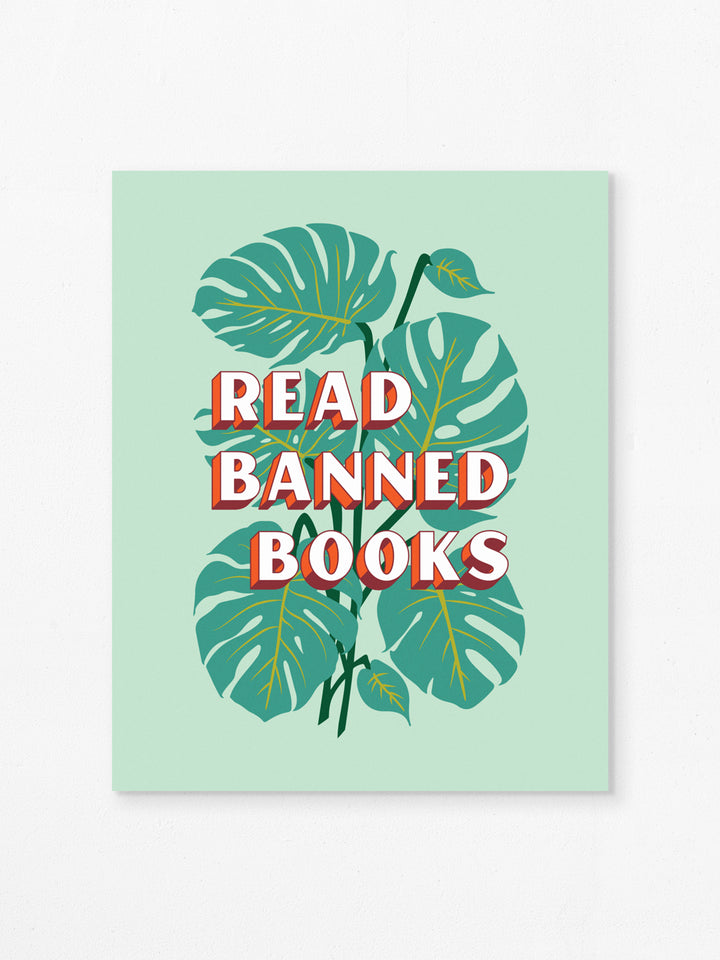 Flat art print on white background. Print features bookish quote, "Read banned books," over illustration of monstera plant leaves on mint green background.