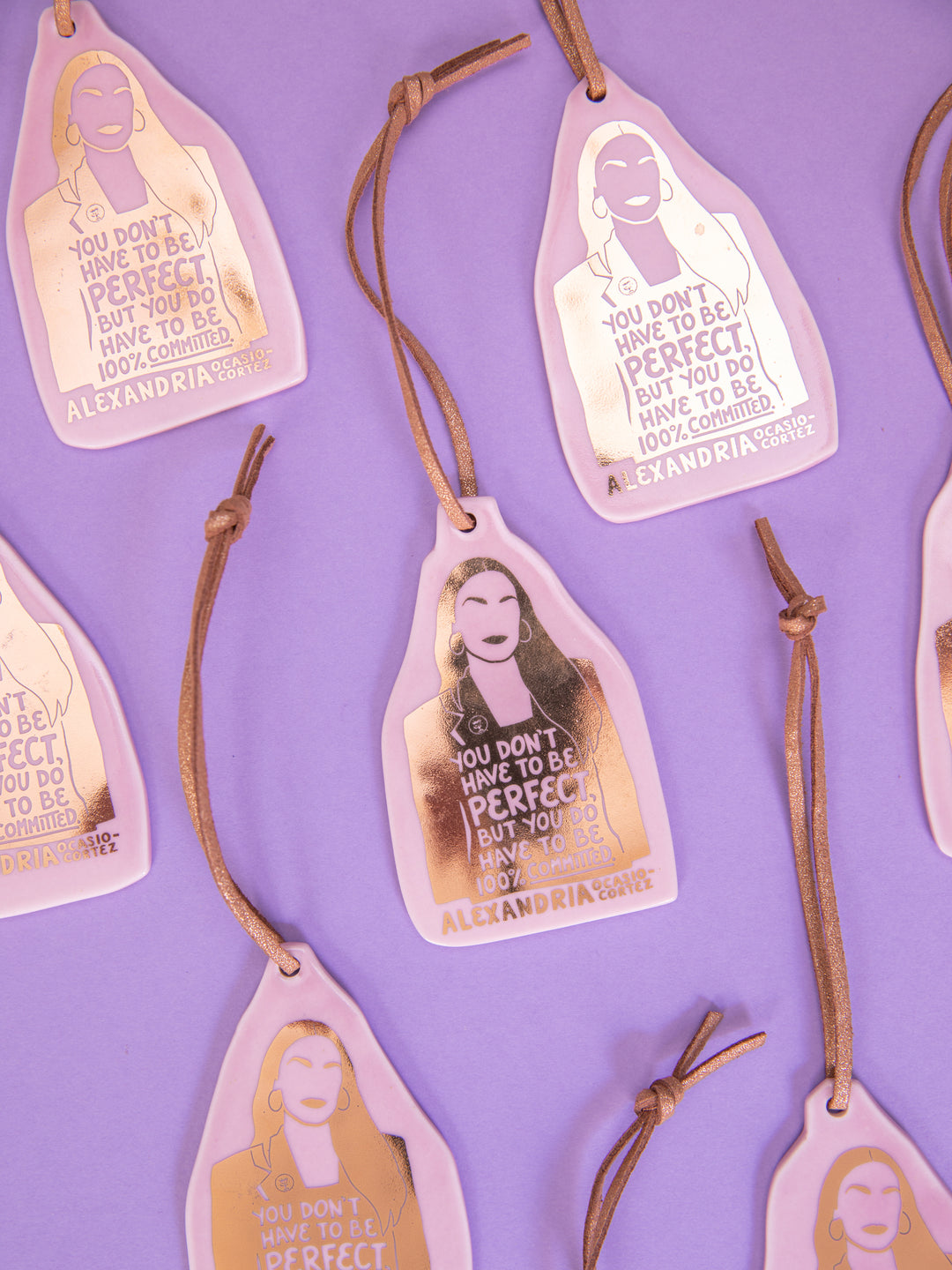 Several Alexandria Ocasio-Cortez ceramic ornaments on purple background. aoc merch