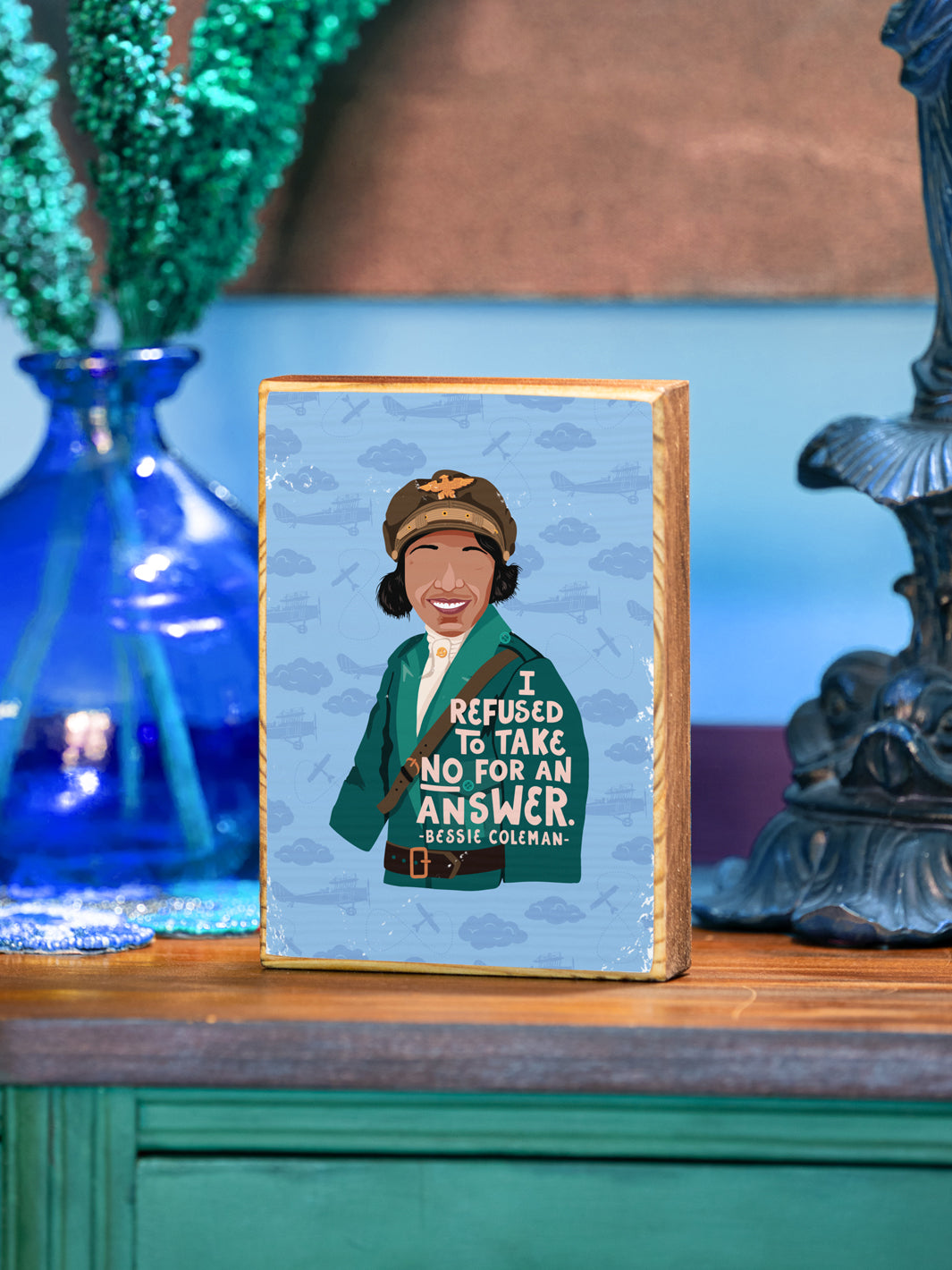 Bessie Coleman, woman pilot, illustration with quote, "I refused to take no for answer." wood art on buffet beside a vase and lamp. Bessie Coleman art