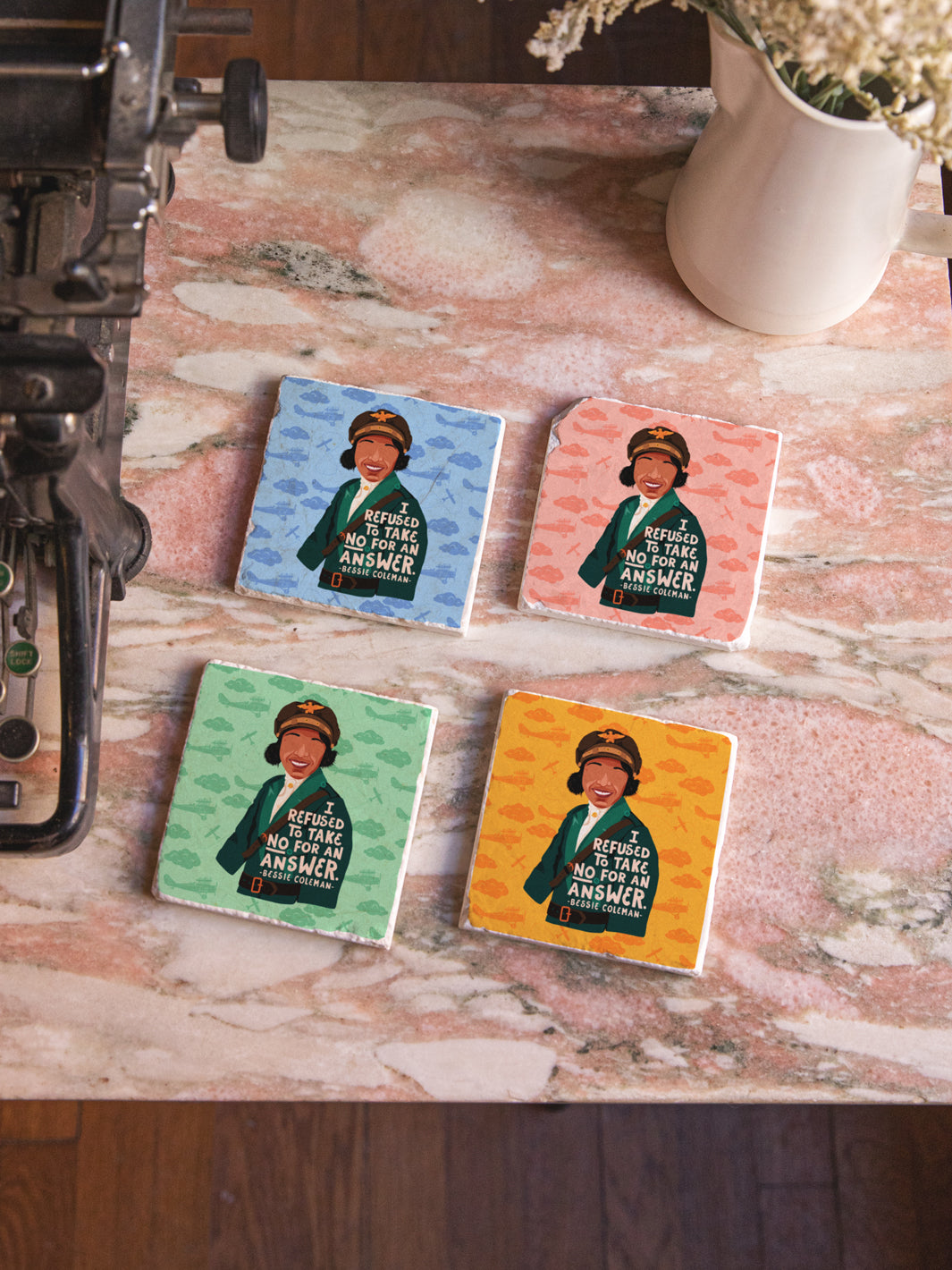 Bessie Coleman, American Aviator, marble coaster set of 4 in light pink, yellow, green and light blue on marble table beside typewriter and flowers. Bessie Coleman art