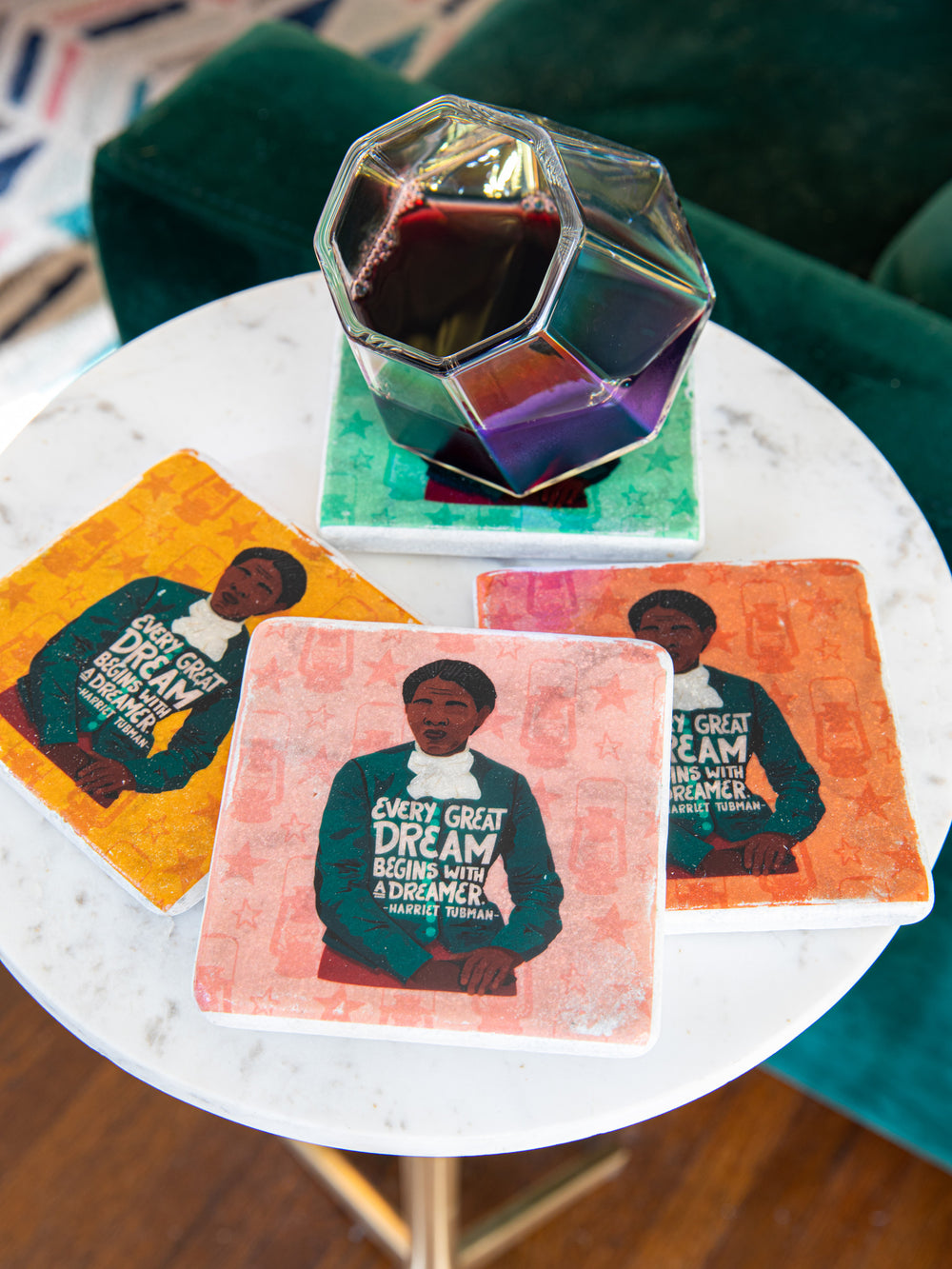 Lifestyle photo of coasters on a white marble tabletop with a glass of wine on top of one the coasters. Harriet Tubman illustration on all coasters. harriet tubman art