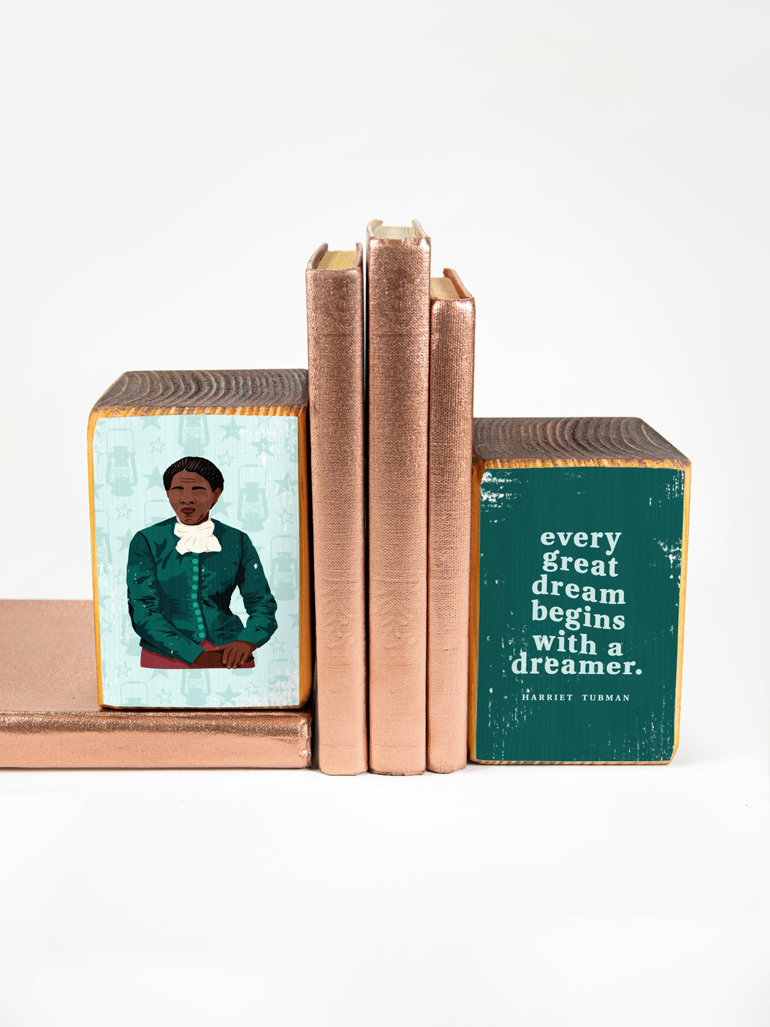 Harriet Tubman bookend set in teal and blue. Left bookend is an illustration of Harriet Tubman. Right bookend is of a Harriet Tubman quote, "every great dream begins with a dreamer." bookends are holding up a stack of metallic copper colored books. harriet tubman art