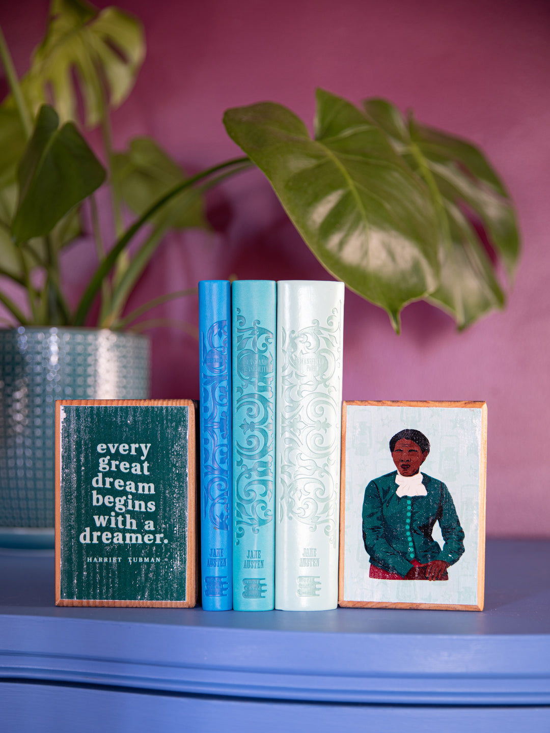 Lifestyle photo of harriet tubman bookends holding up a stack of 3 blue books. Plants in the background. harriet tubman art