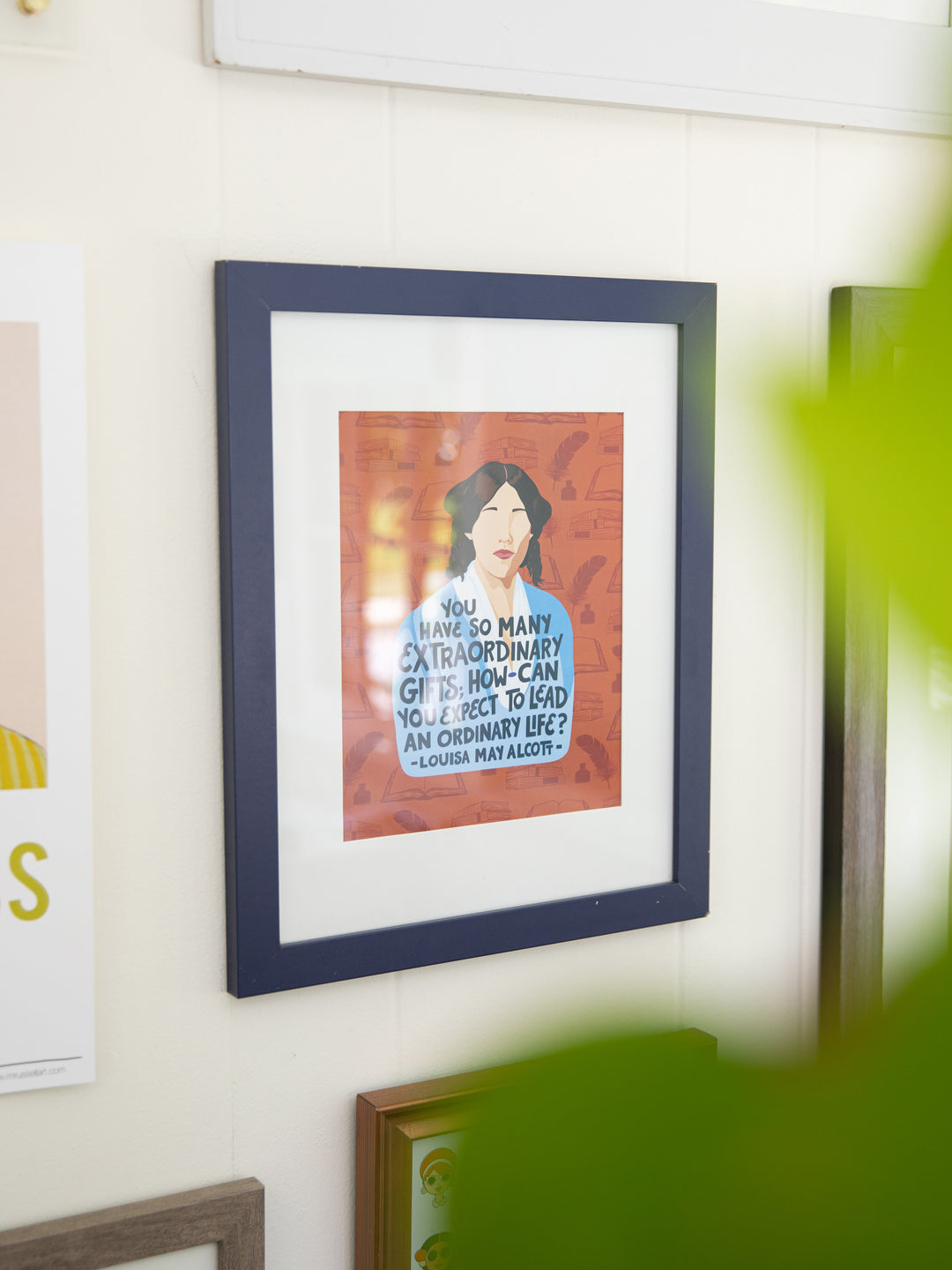 Louisa May Alcott illustrated 8x10 art print on white wall in navy frame with white matte, plant in the foreground. Louisa May Alcott gifts