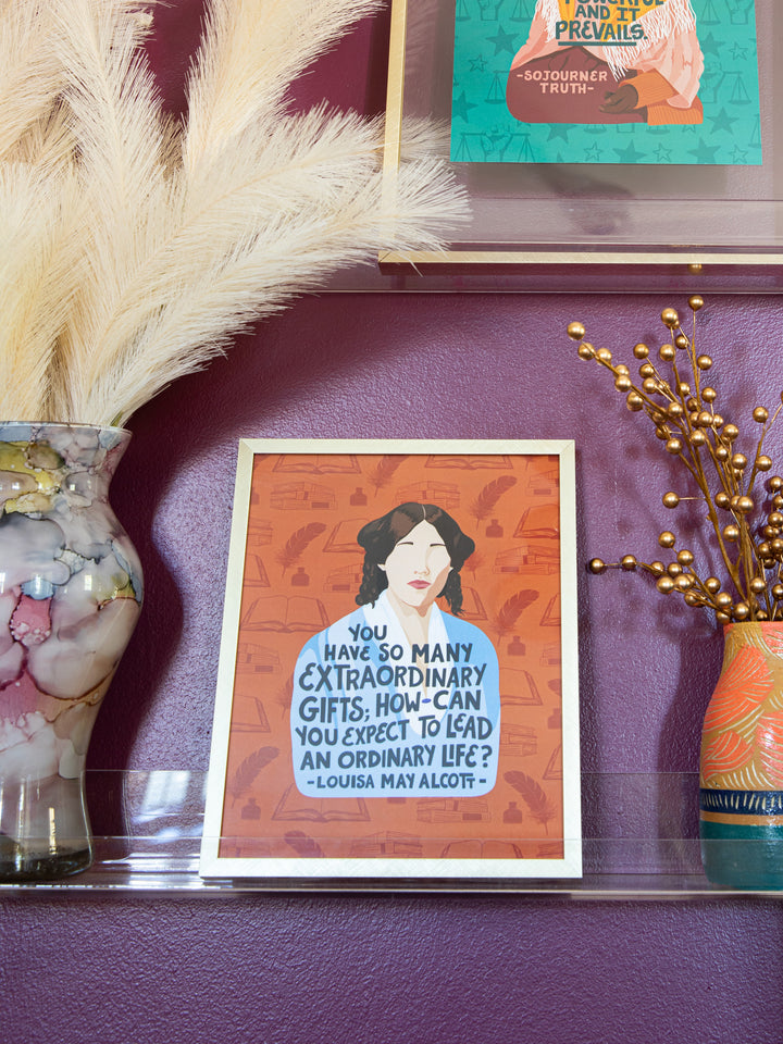 Louisa May Alcott illustrated 8x10 art print in gold frame leaning against purple wall on acrylic shelf between two vases