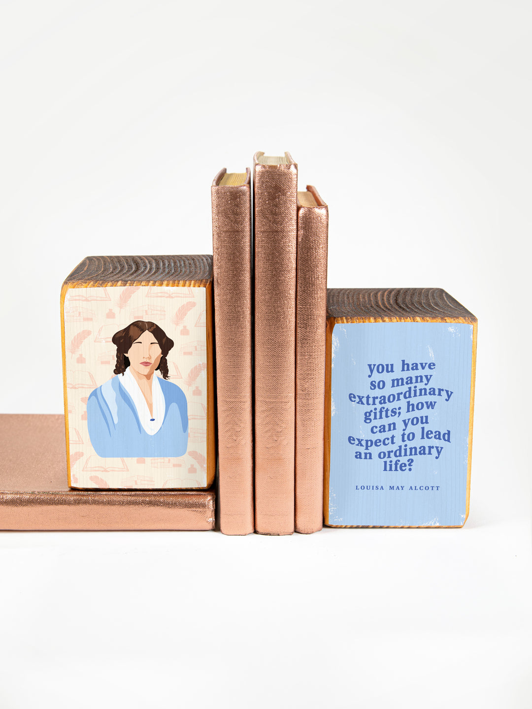 Wood bookends featuring original illustration of American novelist and author of Little Women, Louisa May Alcott, paired with Jo March quote, "You have so many extraordinary gifts; how can you expect to lead an ordinary life?" on a white background with copper books. Louisa May Alcott gifts