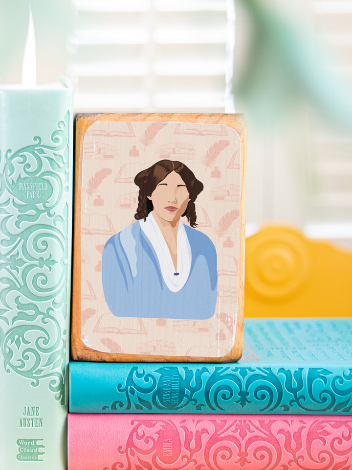 Wood bookends featuring original illustration of American novelist and author of Little Women, Louisa May Alcott, paired with Jo March quote, "You have so many extraordinary gifts; how can you expect to lead an ordinary life?" beside and on top of colorful books, close up of Louisa illustration. Louisa May Alcott gifts