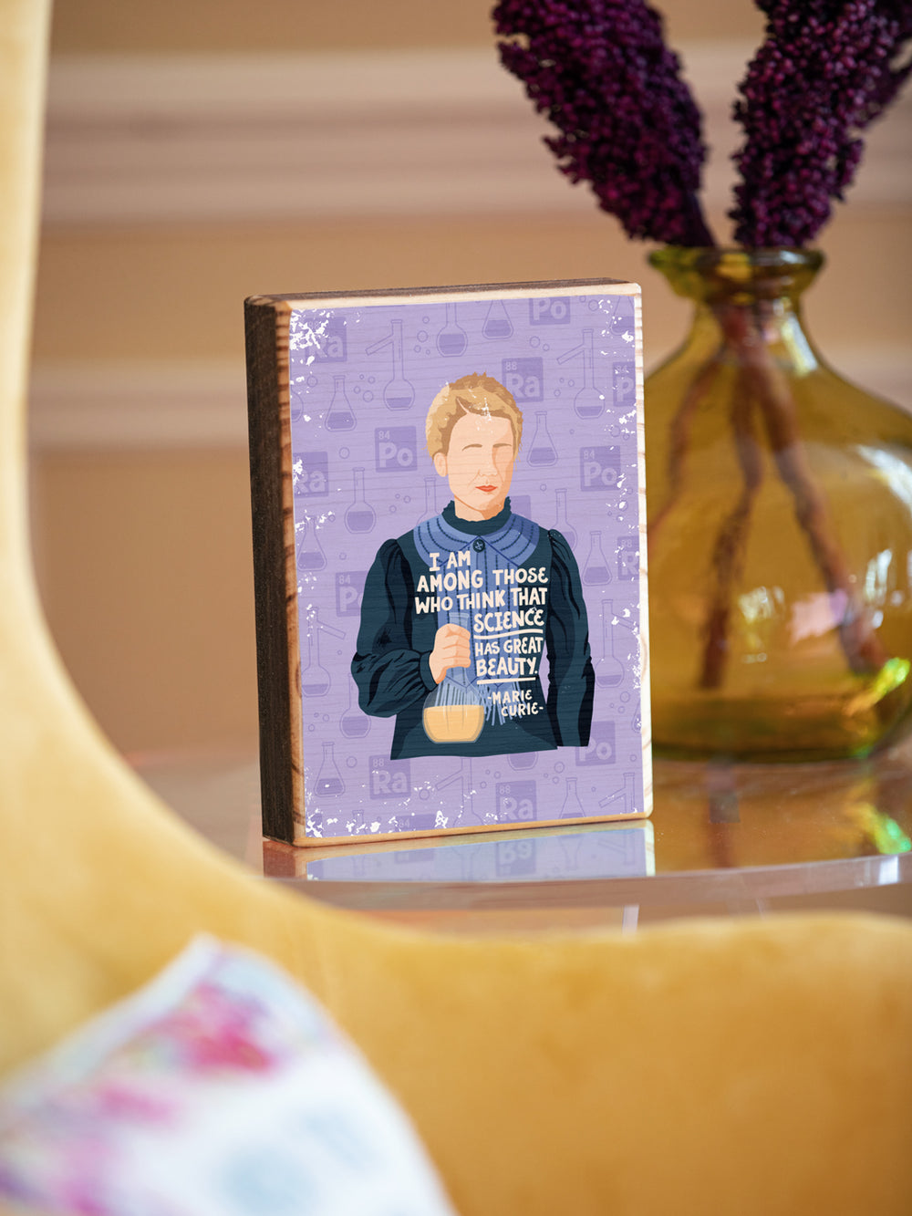 Marie Curie illustration and quote, "I am among those who think that science has great beauty." image transfer on wood on a clear side table beside a yellow chair. Marie Curie art