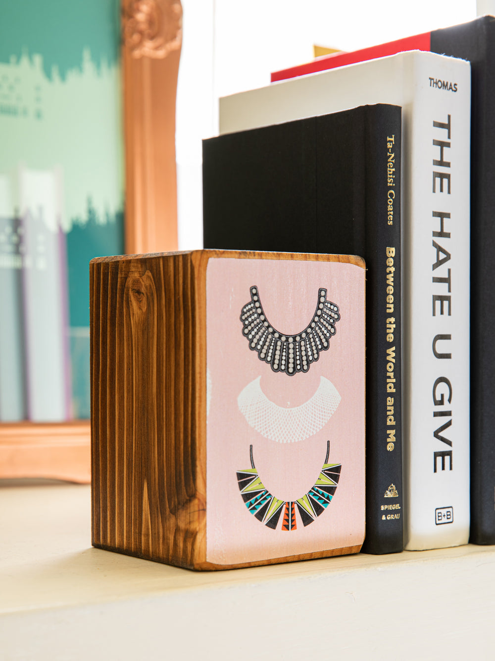 Close up of left side of wood bookend set with illustration of three of Ruth Bader Ginsburg's dissent collars on pink background. Ruth Bader Ginsburg art