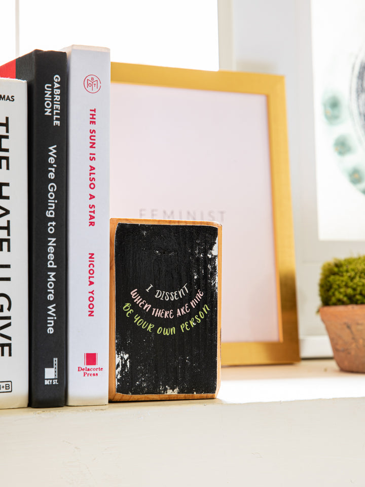 Close up right side of wood bookend set with Ruth Bader Ginsburg sayings, "I dissent," "When there are nine," and "Be your own person," on black background. Ruth Bader Ginsburg art