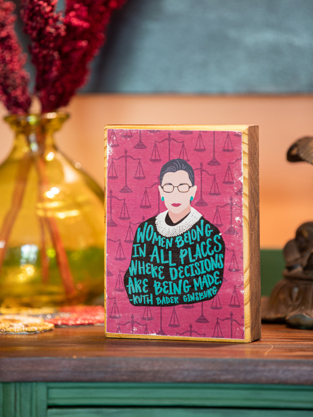 Feminist home decor wood wall art featuring illustration of Ruth Bader Ginsburg (RBG) and quote, "Women belong in all places where decisions are being made." Features magenta/purple background will drawings of justice scales. Ruth Bader Ginsburg art