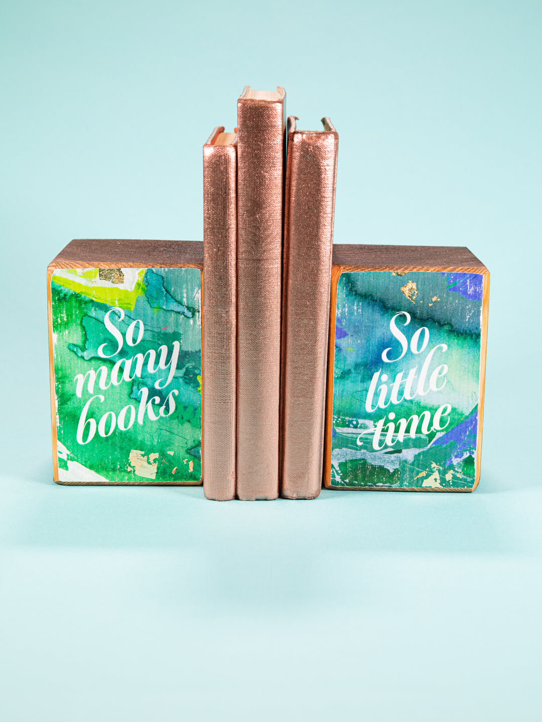 So Many Books So Little Time bookend set by ARCHd and Whitney Winkler Art holding up 3 gold books on a light blue background